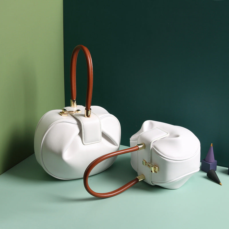 two white leather dumpling handbag with a buckle closure and a single handle, displayed against a two-tone background 