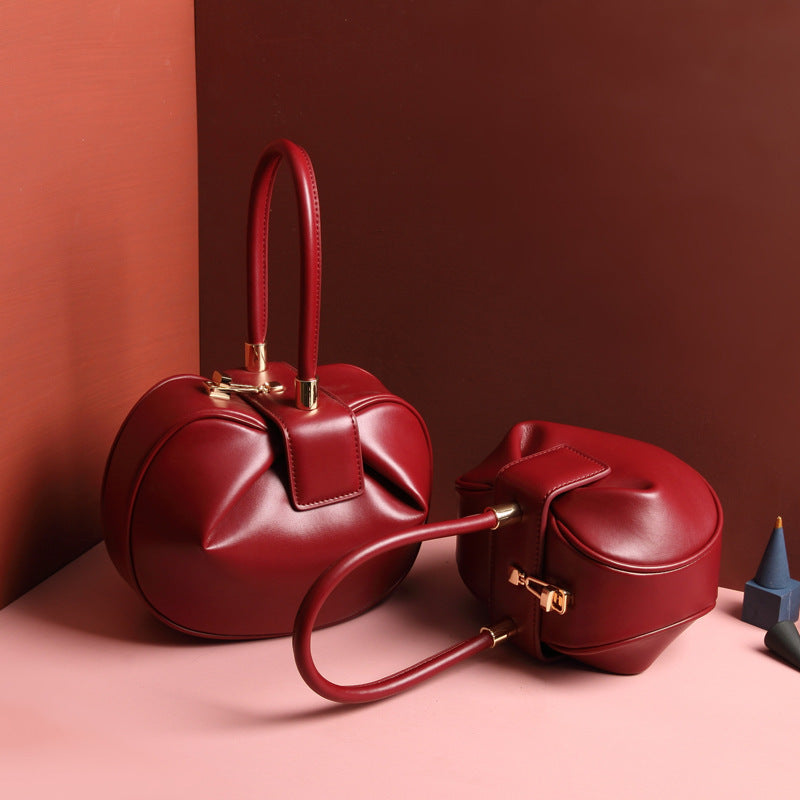 two red leather dumpling handbag with a buckle closure and a single handle, displayed against a two-tone background