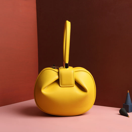 A yellow leather dumpling handbag with a buckle closure and a single handle, displayed against a two-tone background with red and pink shades.