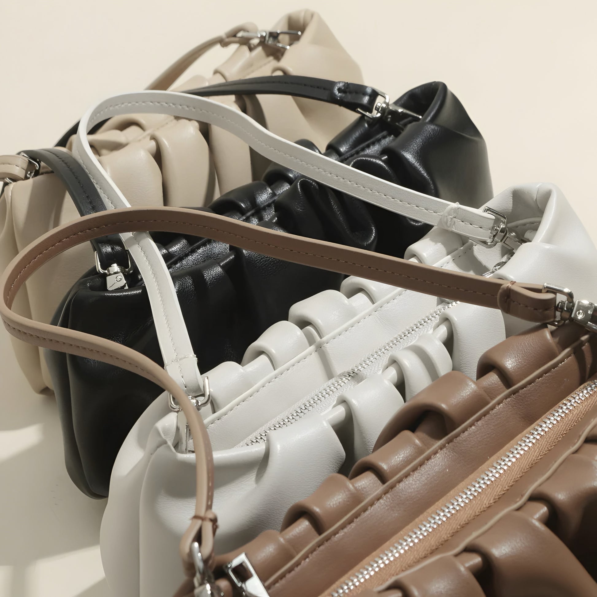 Collection of Genuine Leather Pleated Dumpling Bag in black, white, beige and brown on a beige background– luxury women’s handbag with zippers on a neutral background