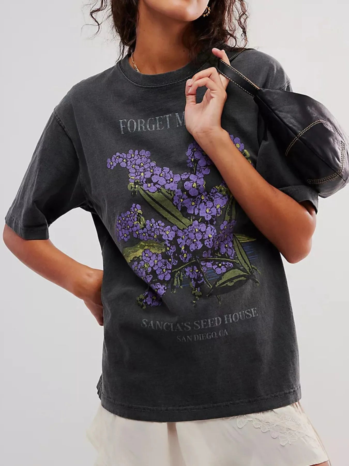 Front view of woman wearing a black loose fit short sleeve t-shirt with purple floral design and text.