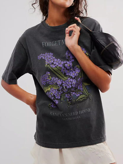 Front view of woman wearing a black loose fit short sleeve t-shirt with purple floral design and text.
