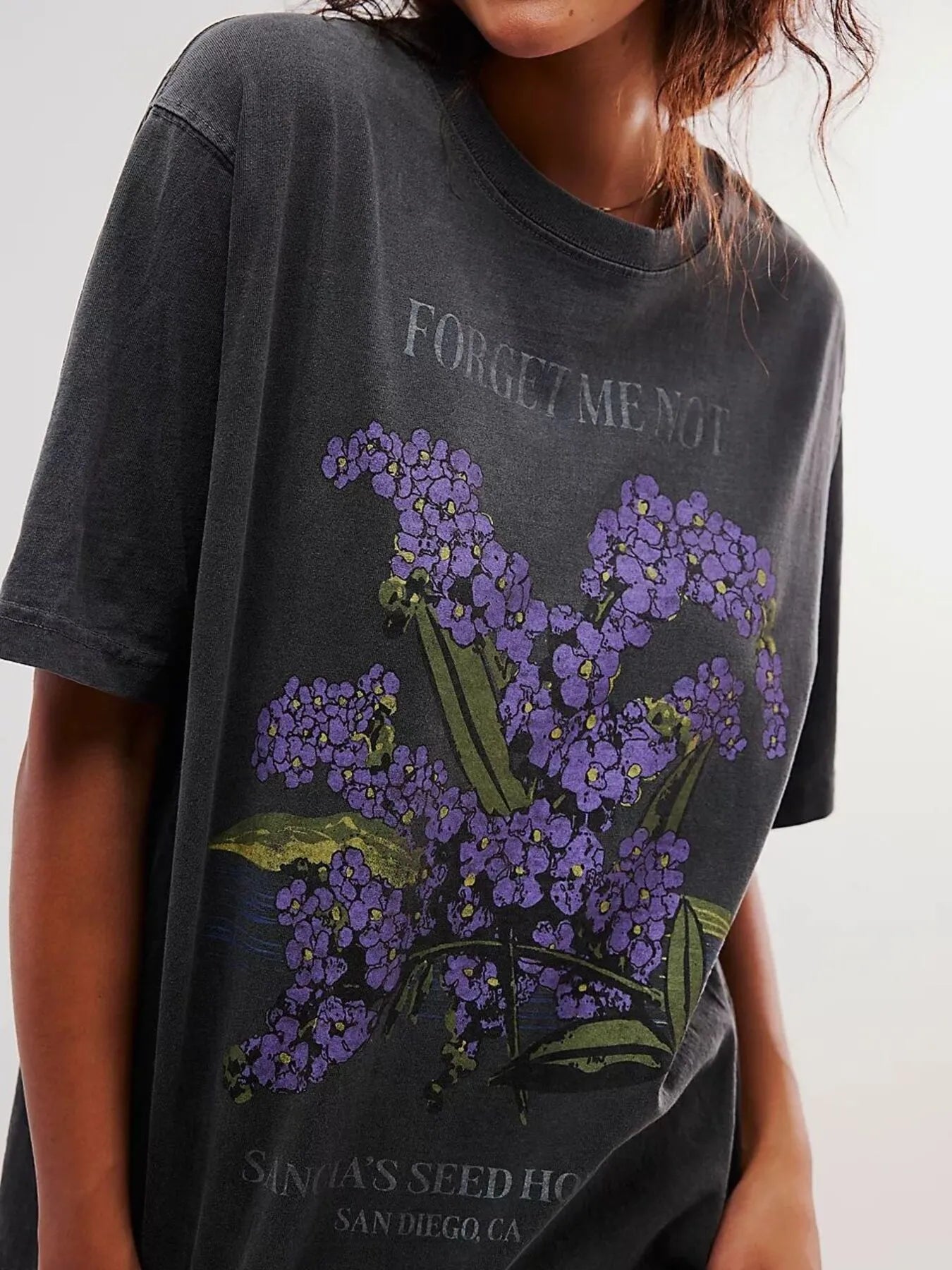 Woman wearing a black short sleeve graphic t-shirt with purple floral design and text