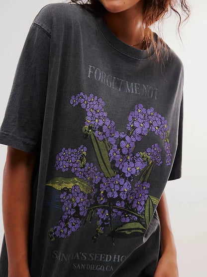 Woman wearing a black short sleeve graphic t-shirt with purple floral design and text