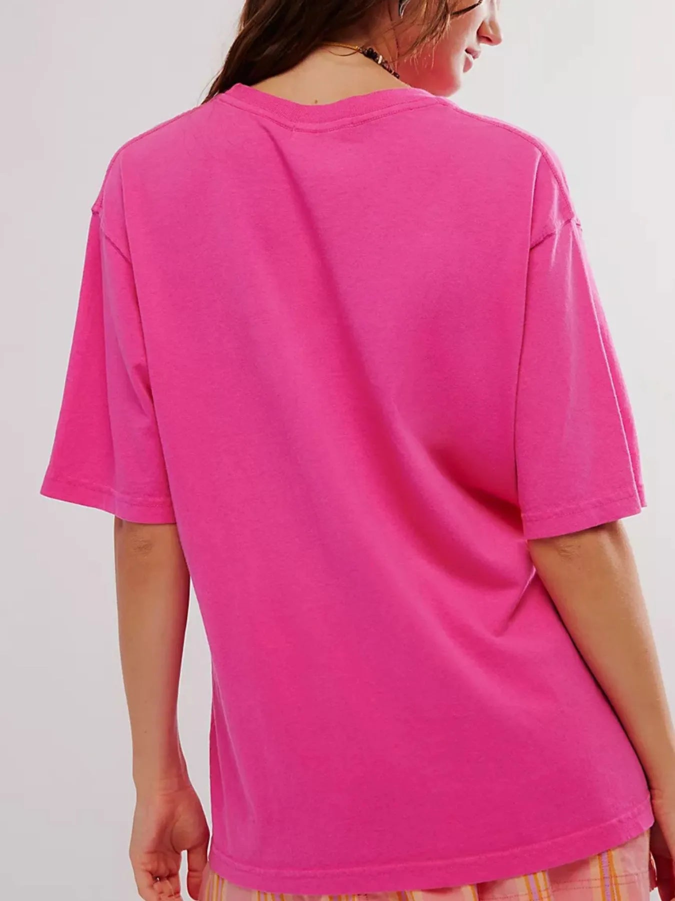 Back view of woman wearing a bright pink t-shirt on a plain background
