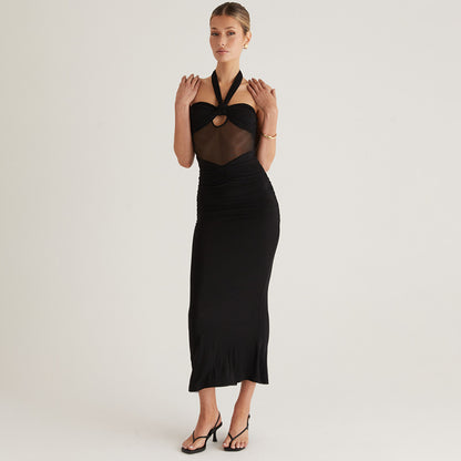 Woman wearing a black knotted halter with sheer bodice maxi evening dress with heels on a plain background
