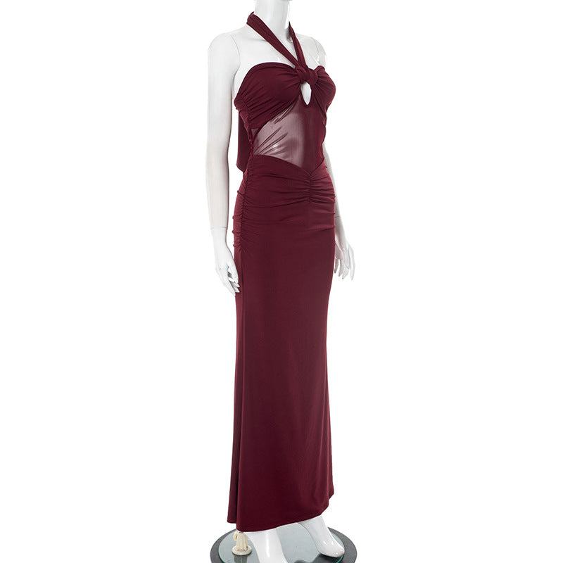 Side view of red/burgundy halter backless evening party dress with sheer bodice on a mannequin against a white background