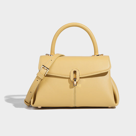 A light yellow satchel leather  handbag with a structured design, featuring a buckle closure, a hand handle, and a detachable strap.