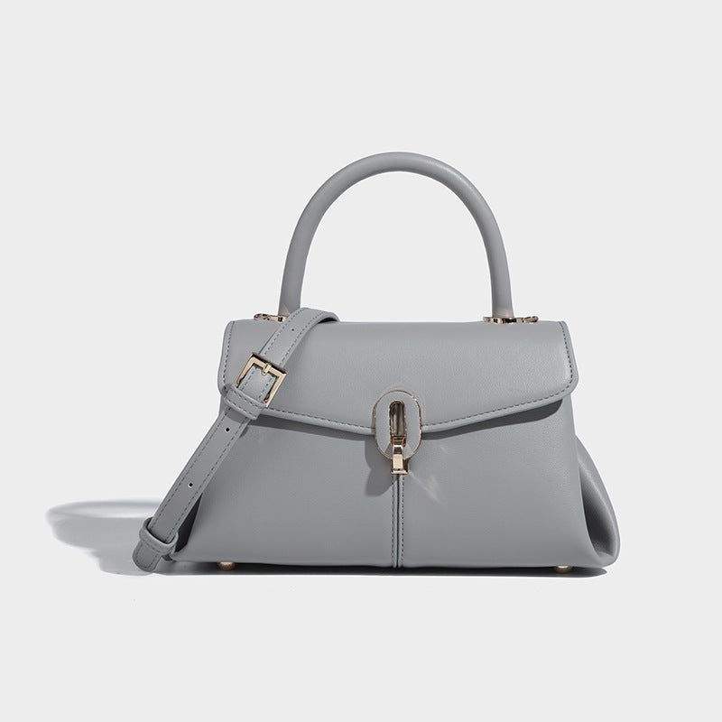 A gray leather satchel handbag with a structured design, featuring a buckle closure, a hand handle, and a detachable strap.