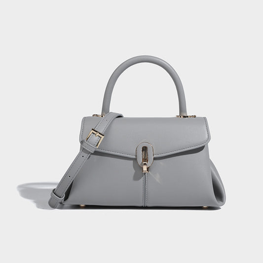 A gray leather satchel handbag with a structured design, featuring a buckle closure, a hand handle, and a detachable strap.