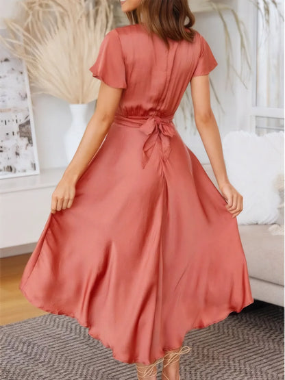 Model walking in coral high-low dress with flutter sleeves and deep v-neckline back view