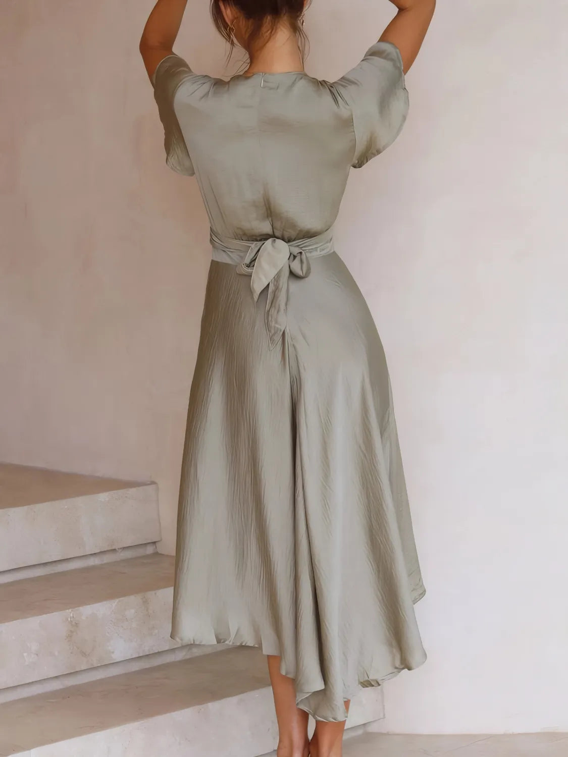 Model wearing in sage high-low dress with flutter sleeves and deep v-neckline back view
