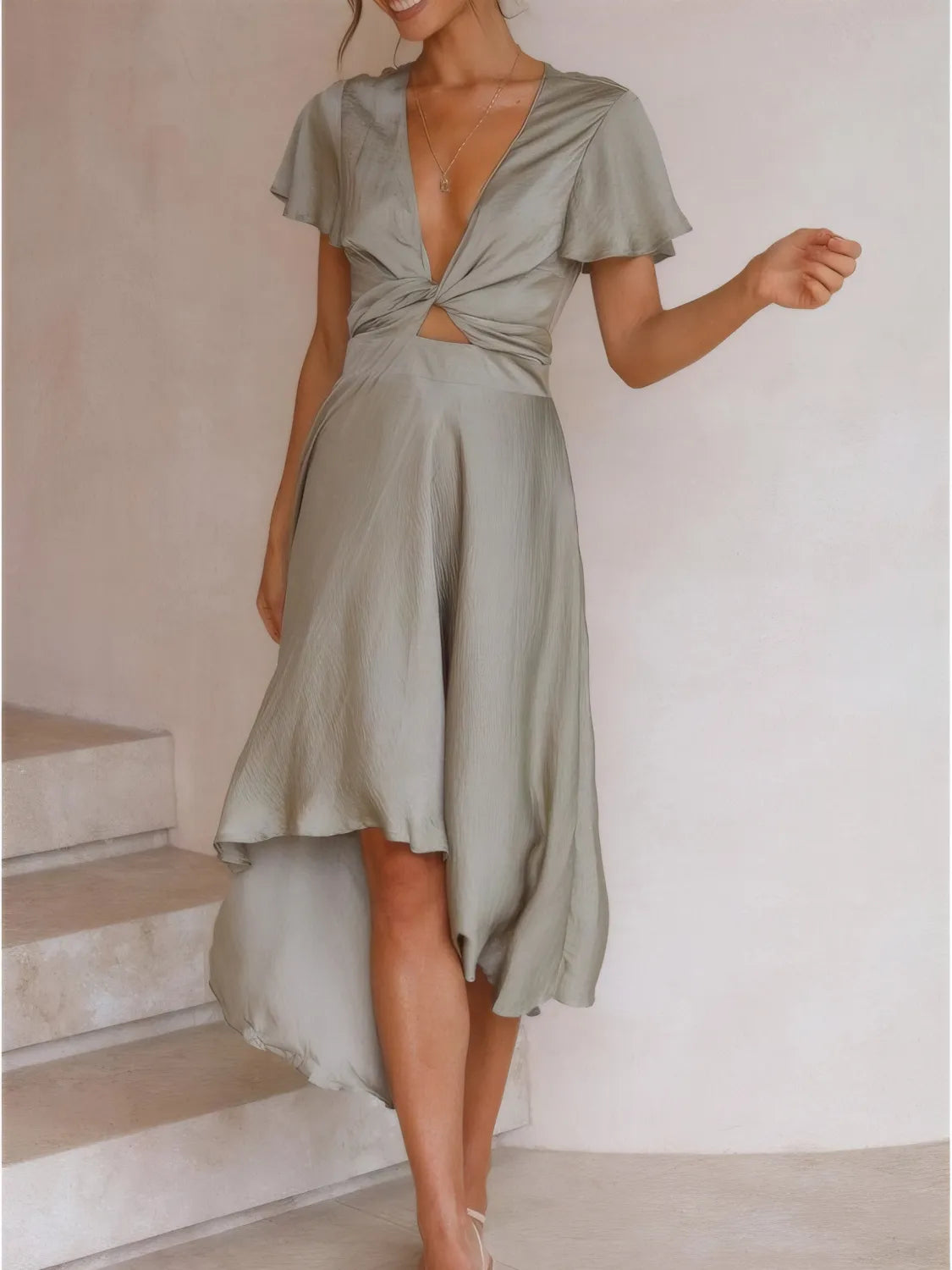 Model walking in sage high-low dress with flutter sleeves and deep v-neckline front view