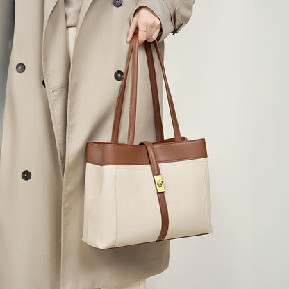 Woman holding a beige and brown contrast genuine leather tote bag with a beige trench coat.