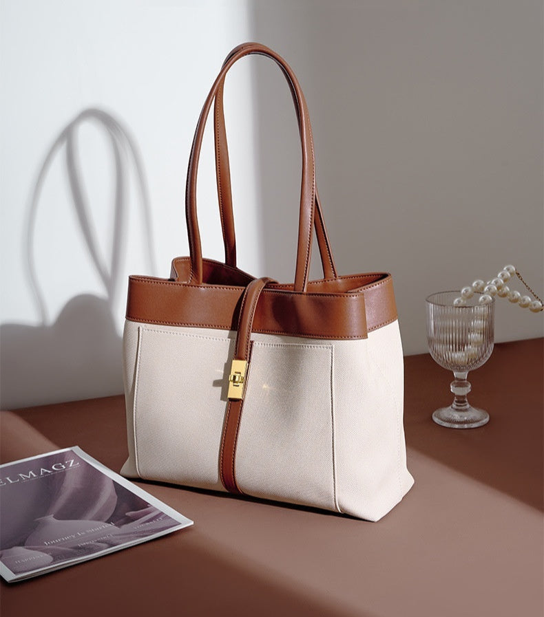 Brown and Beige genuine leather tote bag on a table with a glass of water and magazine.