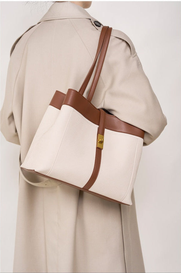 Beige tote bag with brown genuine leather straps worn by a woman with a beige trench coat.