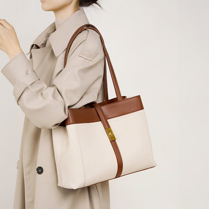 Woman wearing a beige trench coat holding a brown and beige genuine leather handbag on a plain background