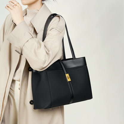 Woman holding a black genuine leather Shoulder bag with a gold clasp against a neutral background