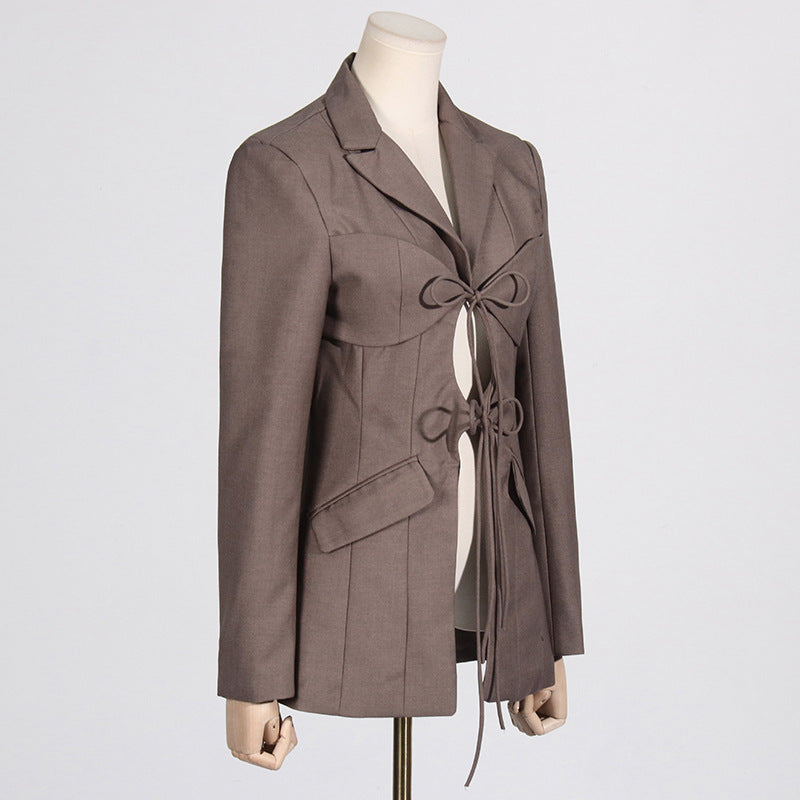 Side view of a luxury fashion inspired  beige/khaki hollow-out cinched irregular  longs sleeve blazer with a deep v-neckline and lace up front detail on a mannequin