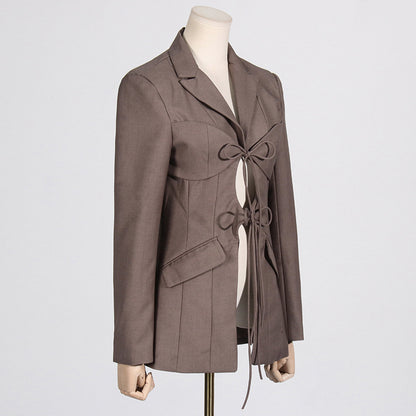 Side view of a luxury fashion inspired  beige/khaki hollow-out cinched irregular  longs sleeve blazer with a deep v-neckline and lace up front detail on a mannequin