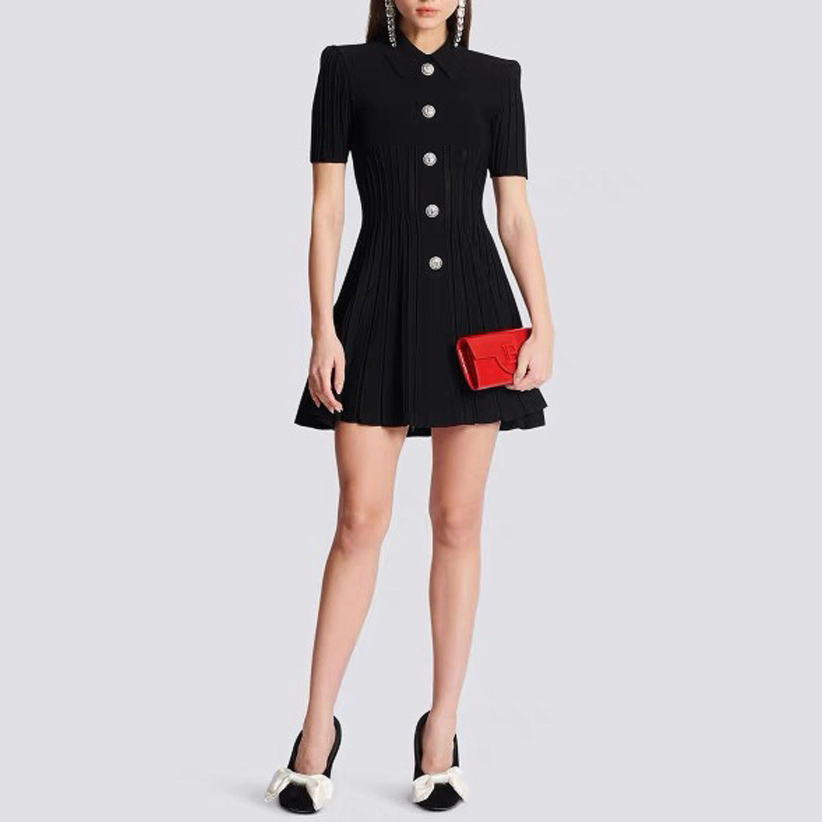 A woman wearing a black A-line knit mini dress made from premium knit fabric with silver statement front buttons on a white background