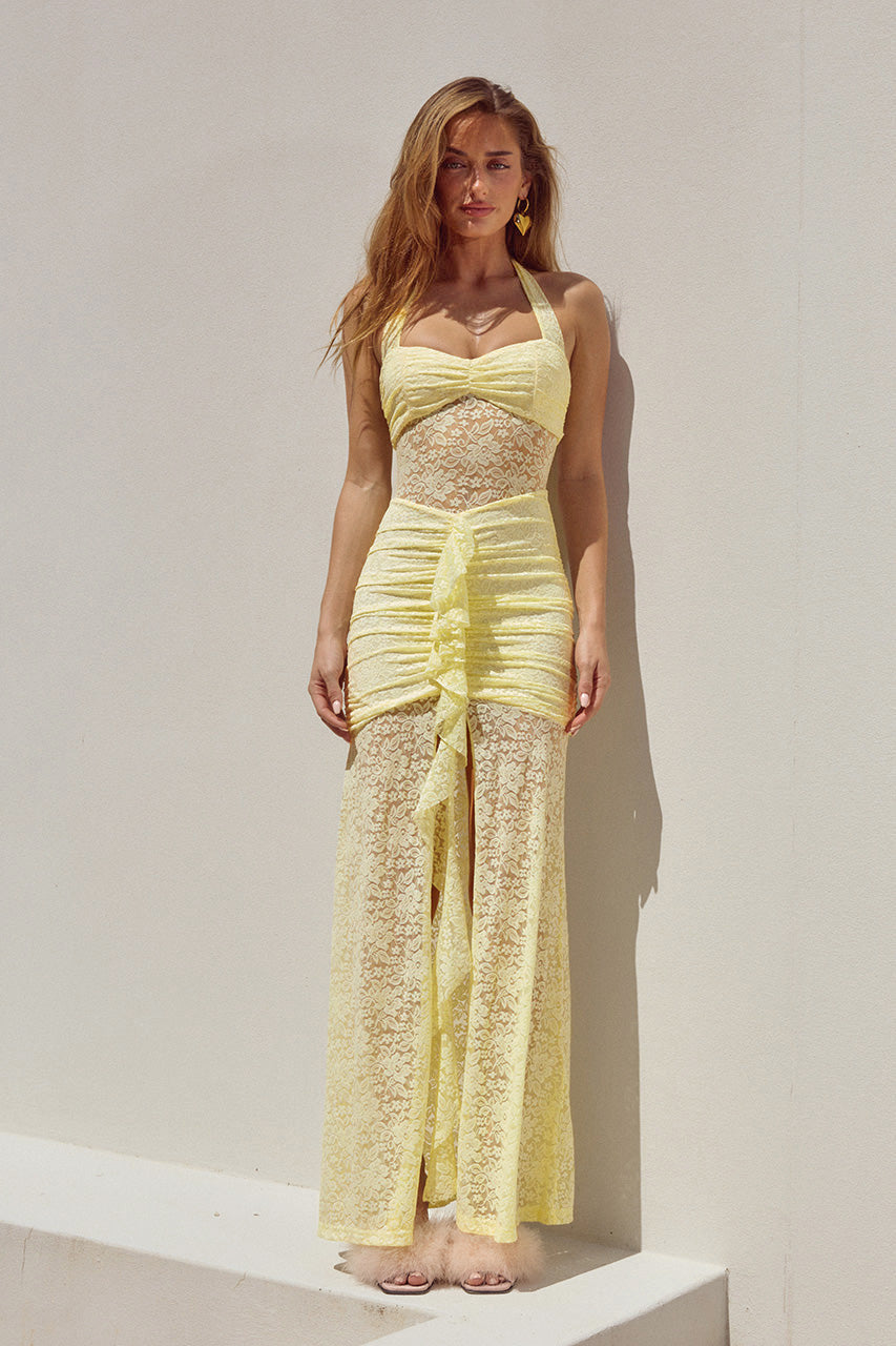Woman wearing a yellow backless halter lace maxi party dress against a white background