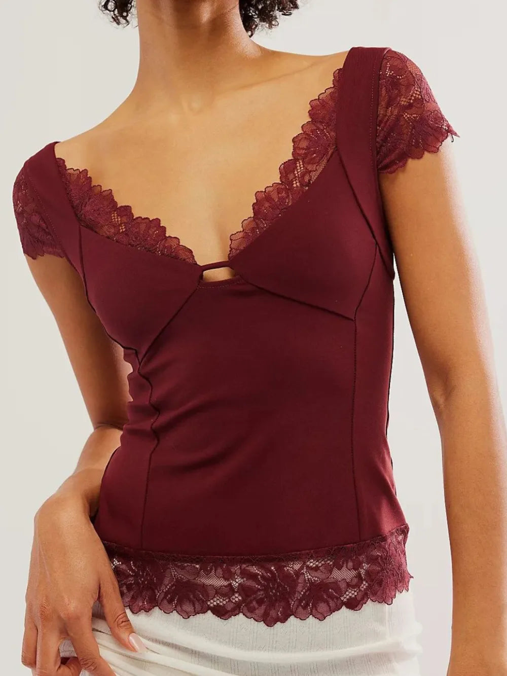 Woman wearing a Maroon/ Burgundy V-neck lace top with cap sleeve on a white background