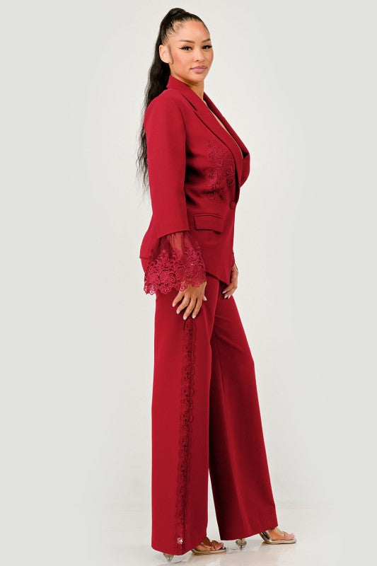 Side view of woman wearing a luxury high fashion burgundy lace blazer and pants set with lace details on a white background