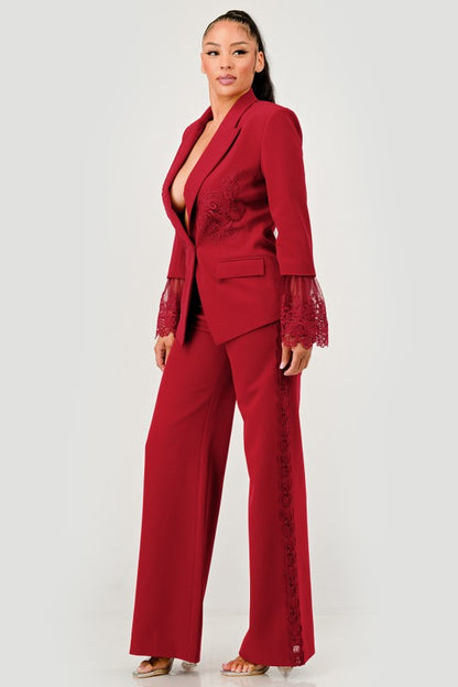 Woman wearing a luxury high fashion burgundy lace blazer and pants set with lace details on a white background
