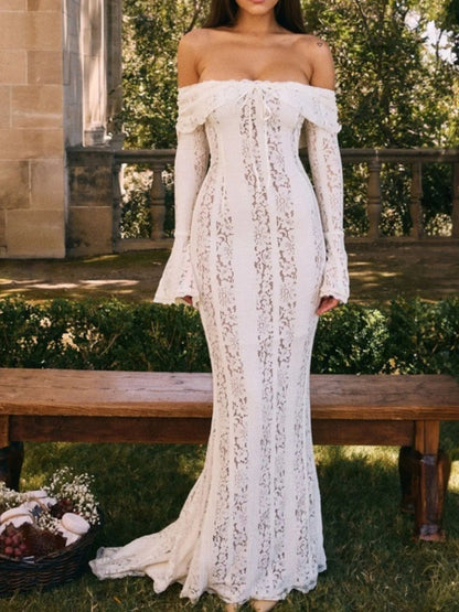 Woman wearing a white lace off-shoulder maxi dress dress standing in front on a wooden bench outdoors.
