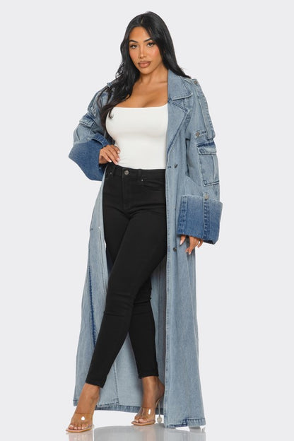 oversized luxe urban style denim trench coat with belted waist, slits , and oversized cuffs styled on a model with black high waist pants and white top