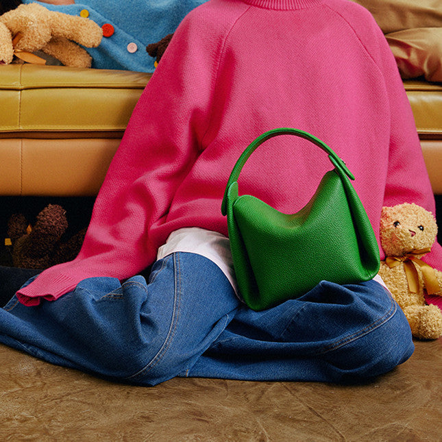 Person wearing a pink sweater and blue jeans sitting on in front of couch with a green Minimalist Genuine Leather Small Bag.