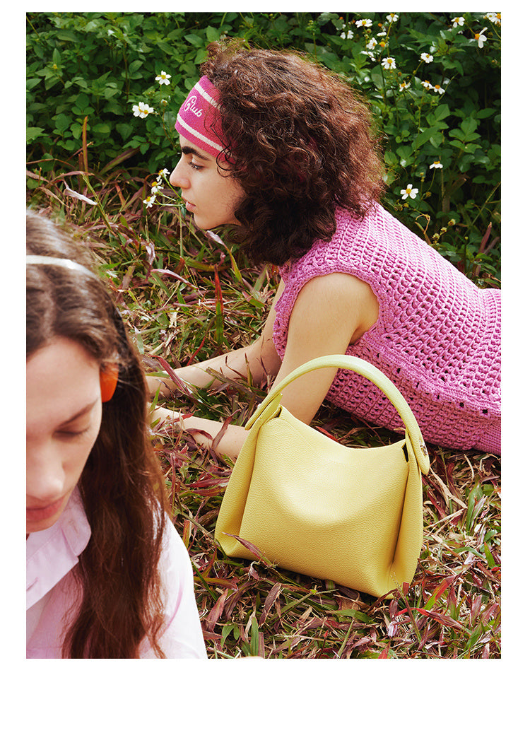 Two women sitting on grass with a yellow Minimalist Genuine Leather Small Bag between them
