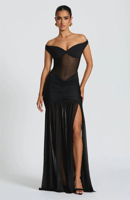 Woman in a black off shoulder backless high thigh slit maxi dress with flowy hem 