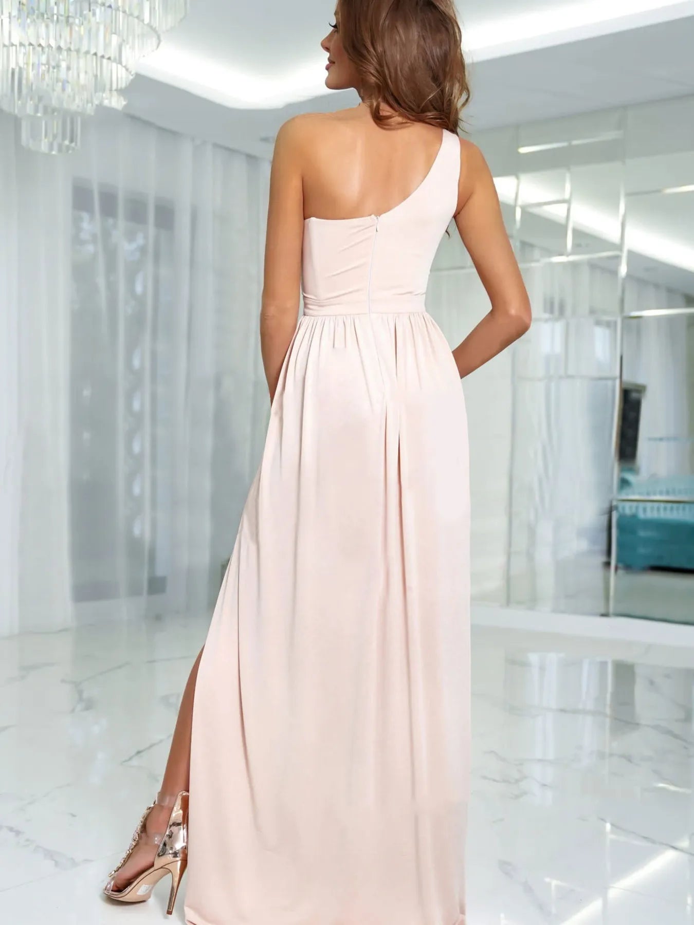 Back view of woman wearing a one-shoulder blush pink maxi elegant evening  dress in a modern interior setting