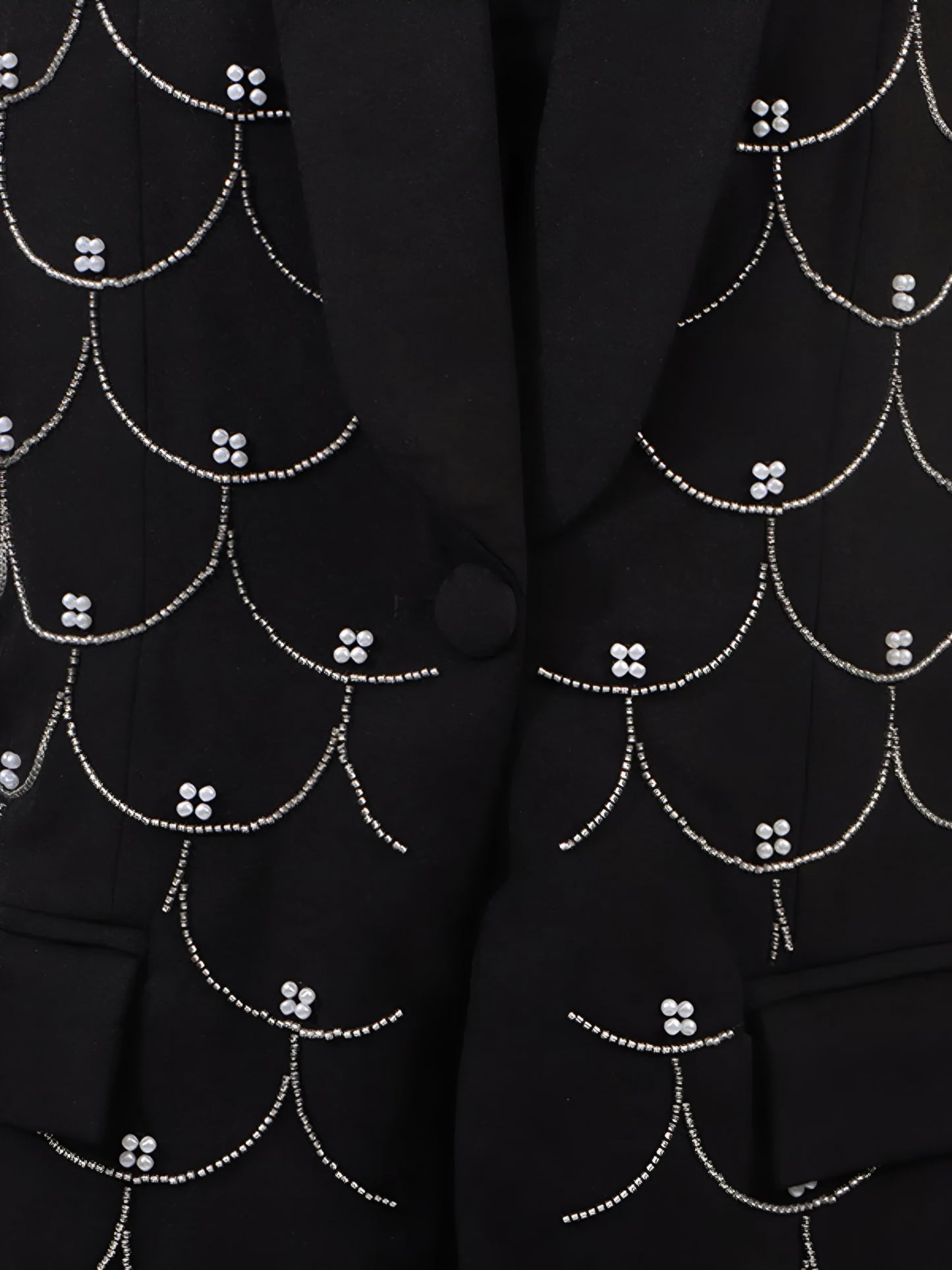 Close up of black blazer with intricate all over white pearl detail patterns and button front