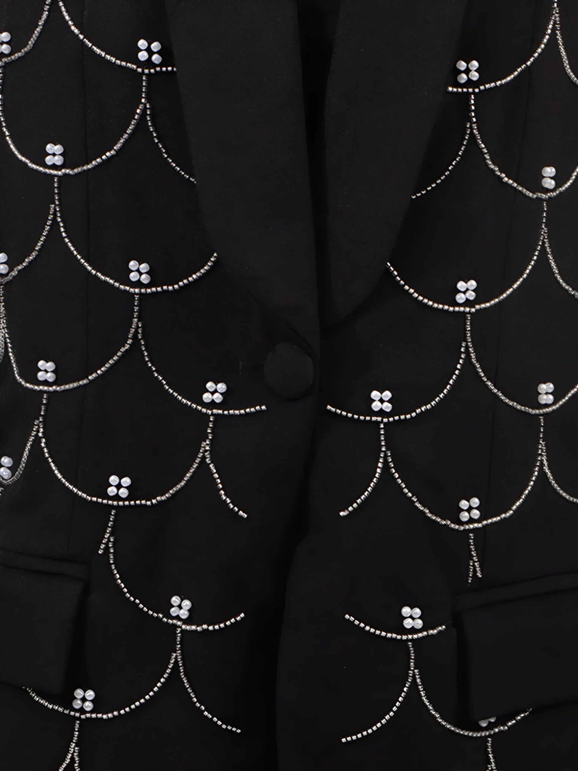 Close up of black blazer with intricate all over white pearl detail patterns and button front