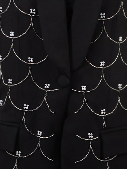 Close up of black blazer with intricate all over white pearl detail patterns and button front