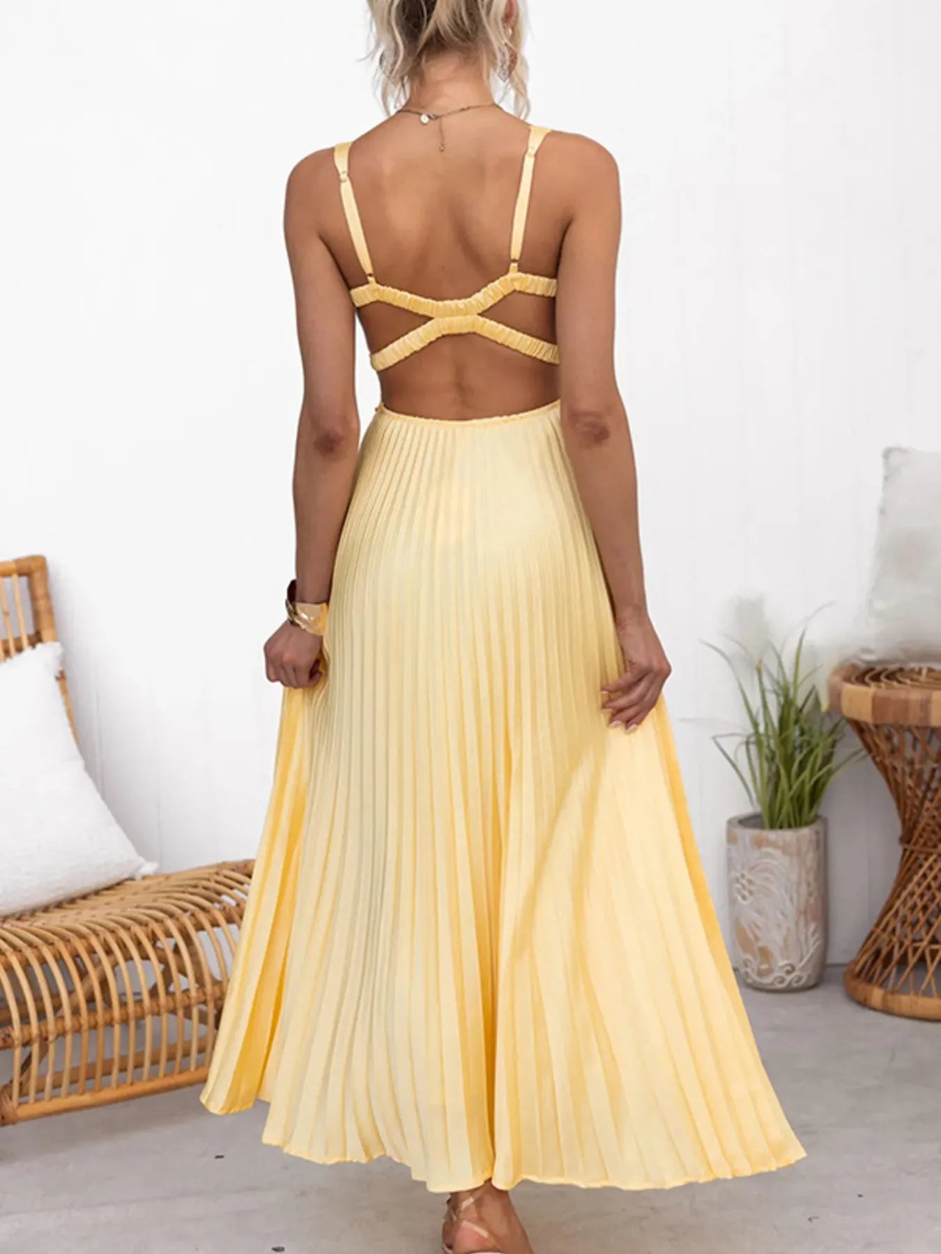 Back view of woman wearing a yellow pleated flowy maxi dress showcasing backless feature . 
