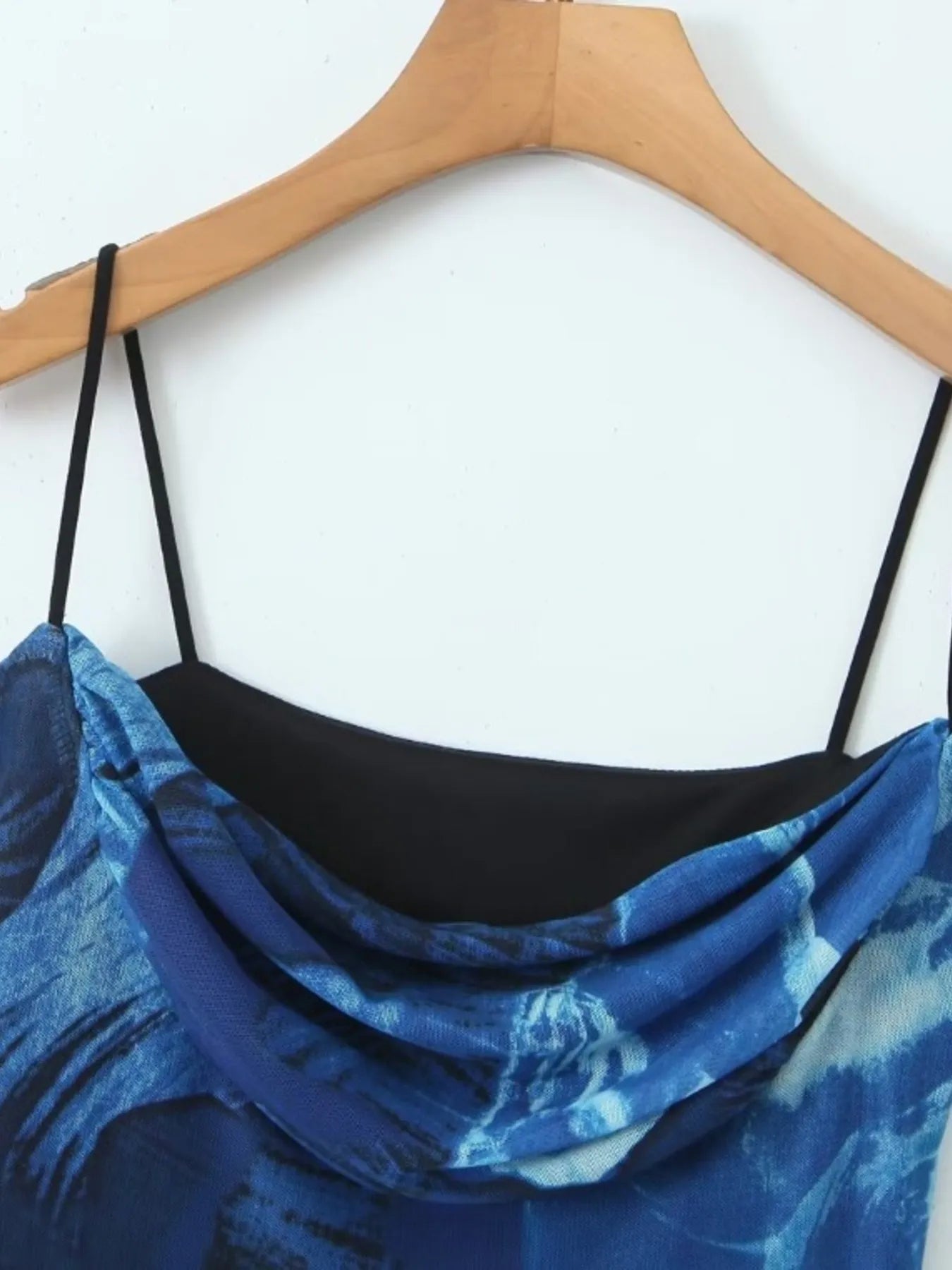 Blue floral printed mini cami dress with black straps on a wooden hanger against a white background