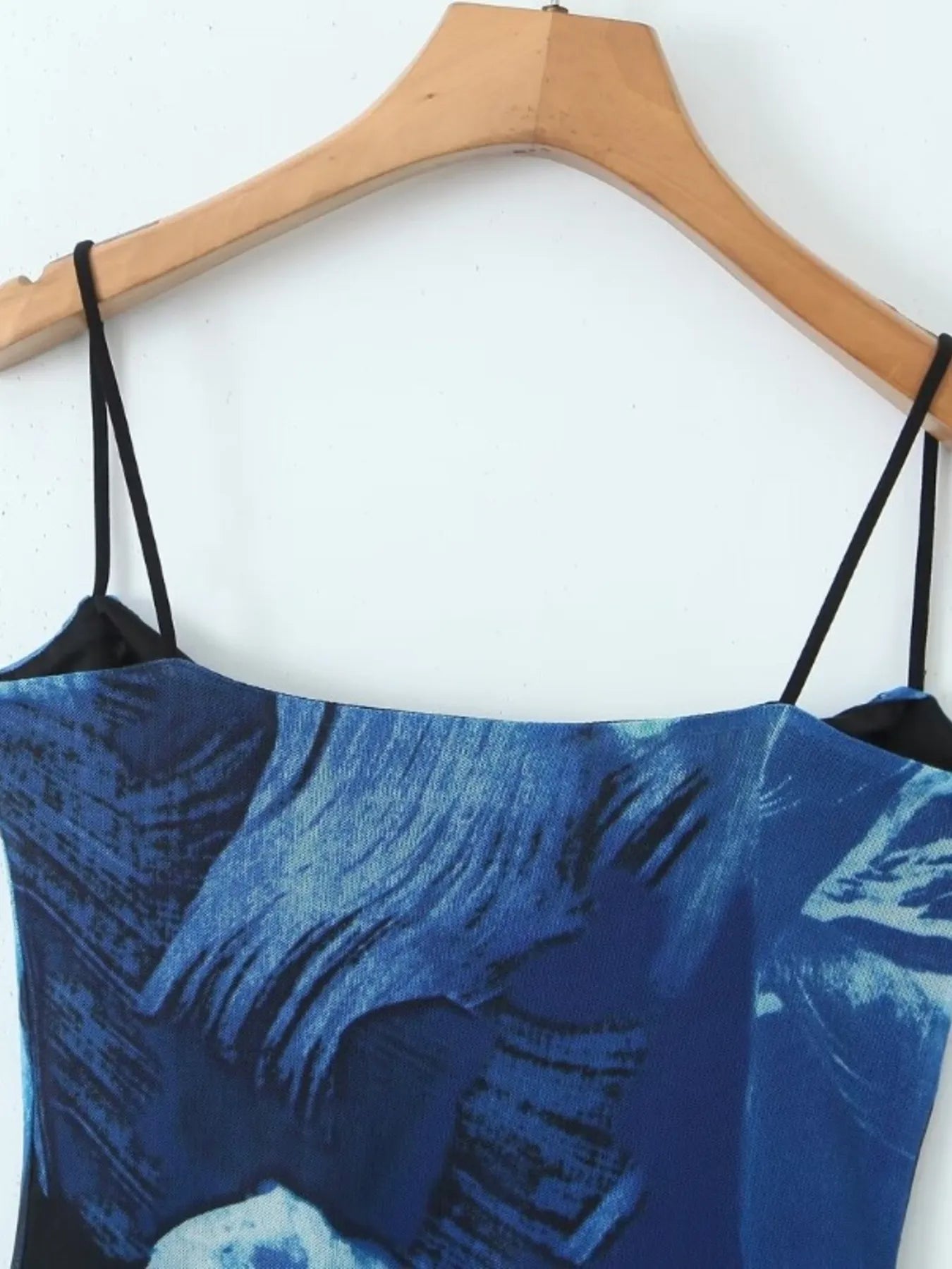 Close up of blue floral mini cami dress black straps on a wooden hanger against a white background
