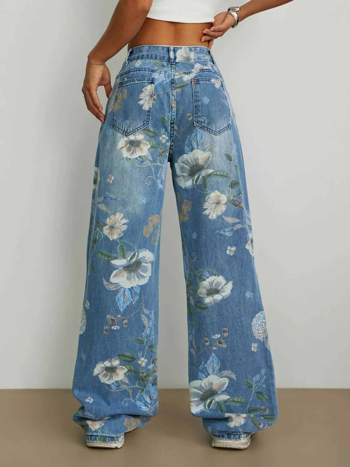 Back view of woman wearing Floral-printed high rise wide leg relaxed jeans  on a plain background
