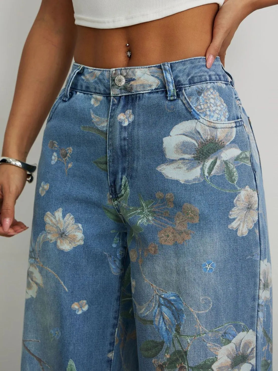 Close up view of Floral-printed wide leg high-waisted relaxed loose jeans worn by a woman on a plain background