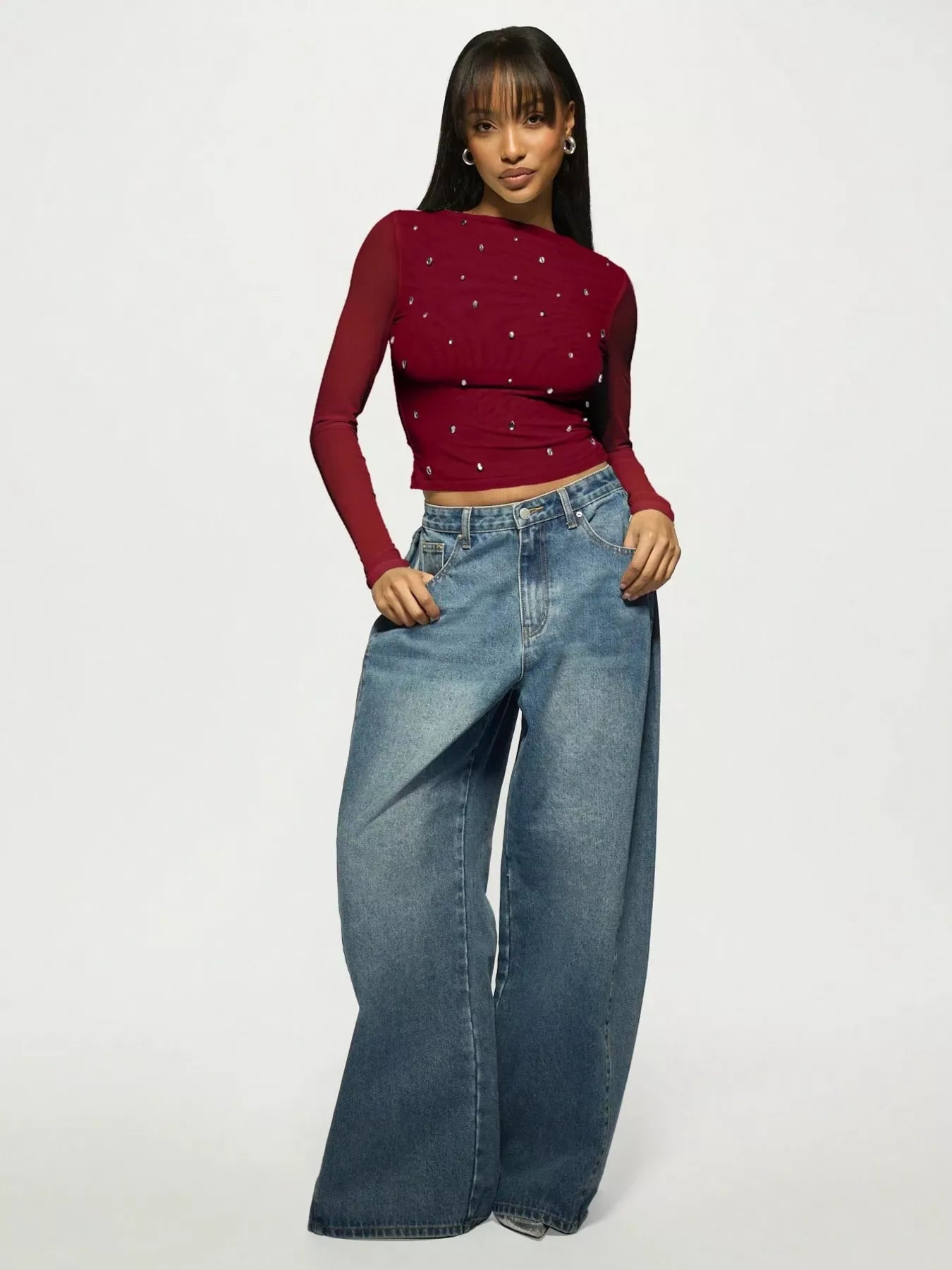 Woman wearing a rhinestone embellished red/burgundy top and blue jeans on a white background