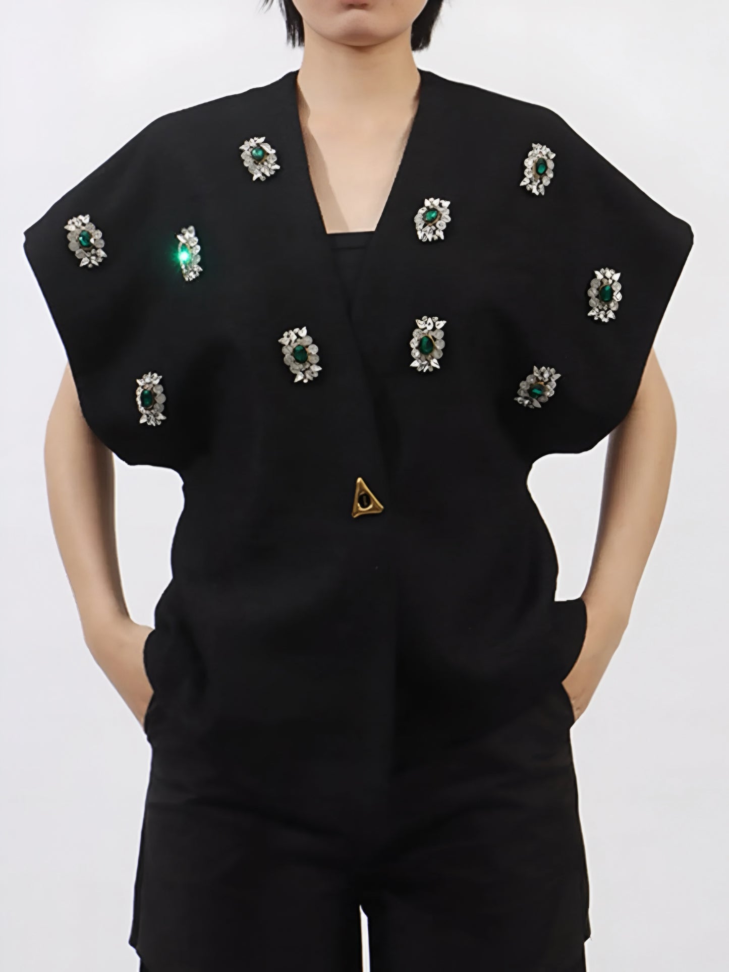 Woman wearing a black luxury vest coat with rhinestone embellishment gemstones on a plain background