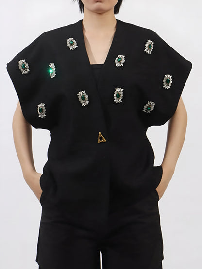 Woman wearing a black luxury vest coat with rhinestone embellishment gemstones on a plain background