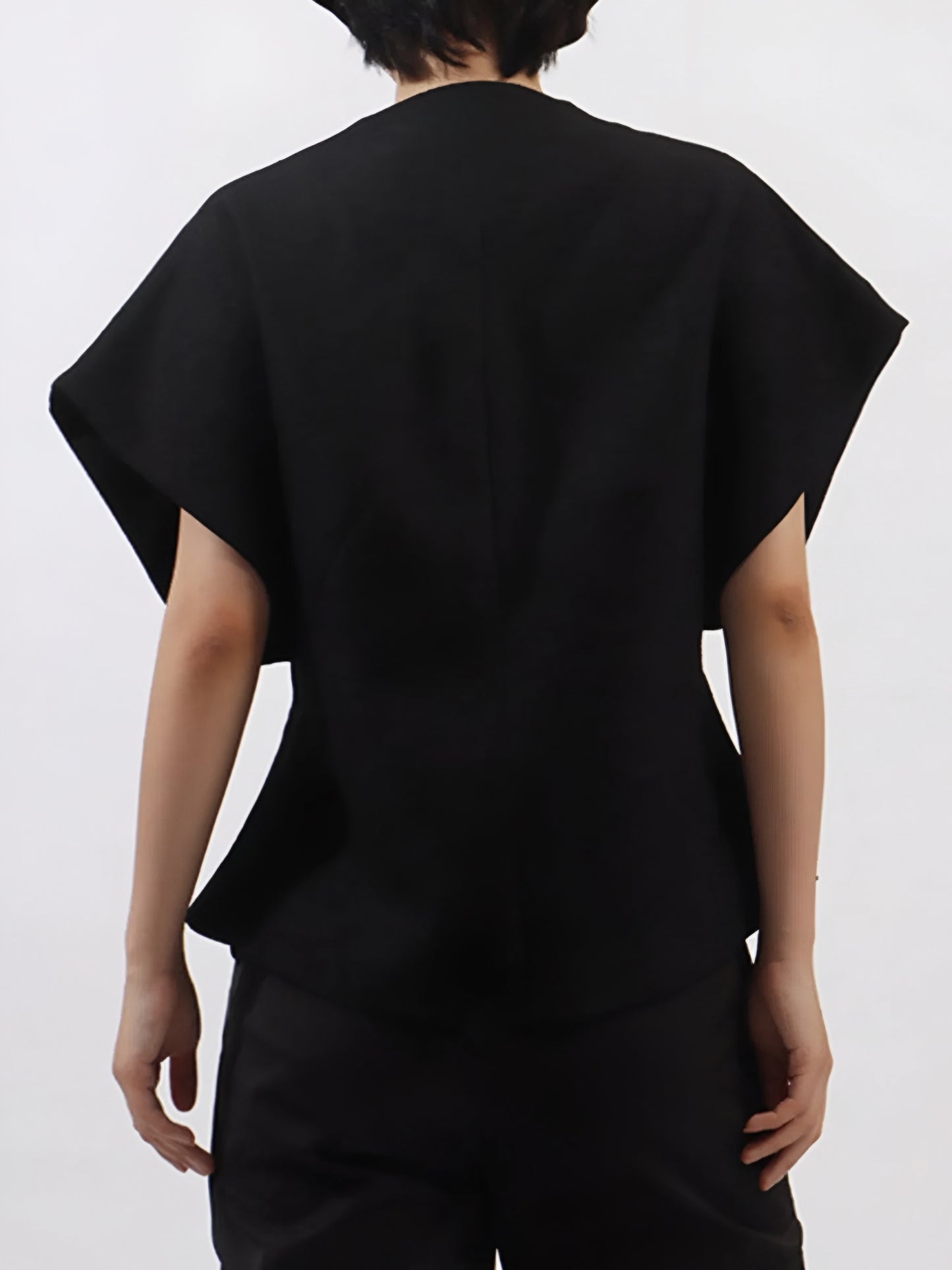 back view of woman wearing a black luxury vest coat with rhinestone embellishment gemstones on a plain background