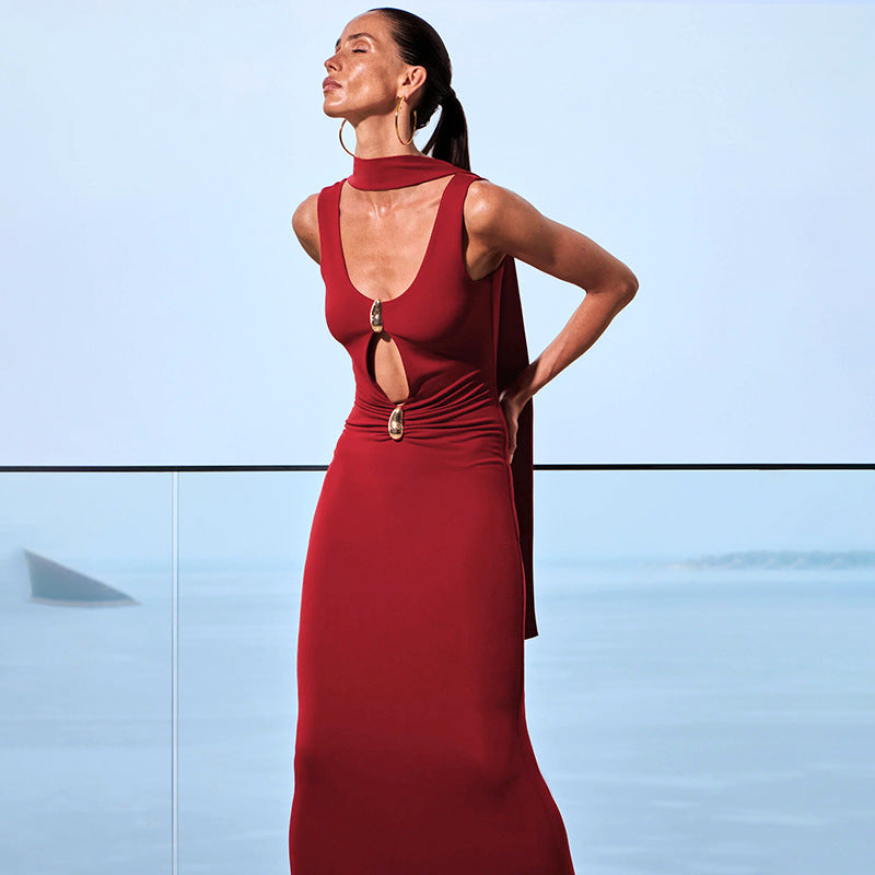 Woman in a red sleek ribbon cut-out maxi dress with gold accent standing against a clear blue sky.