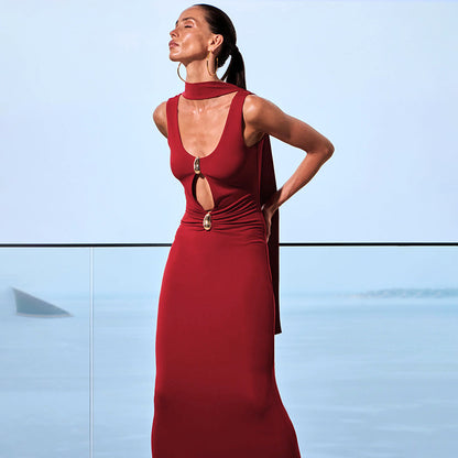 Woman in a red sleek ribbon cut-out maxi dress with gold accent standing against a clear blue sky.