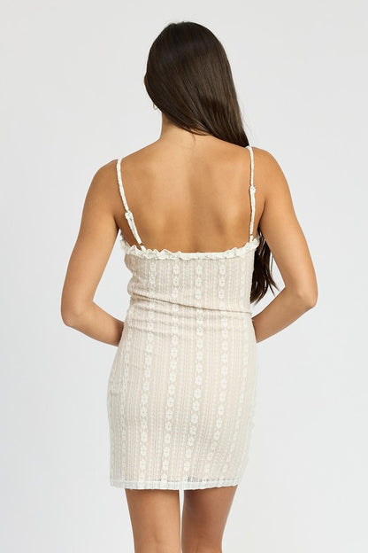 Woman wearing a white lace mini dress with ruffle trim v-neckline and adjustable straps on a white background back view